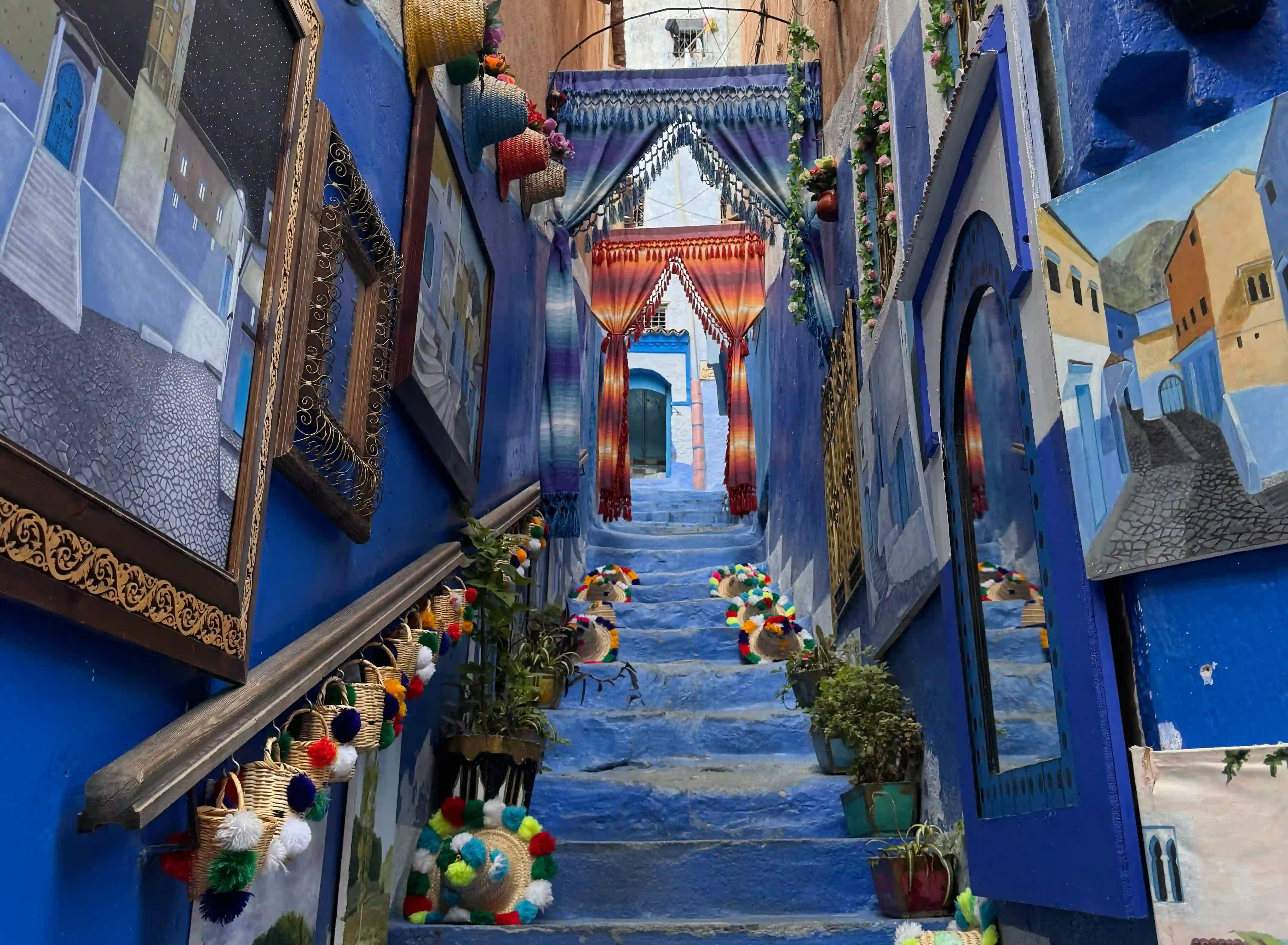 Blue painted staircase lined with colourful woven baskets in a Chefchaouen medina alley, Rif mountains, Morocco