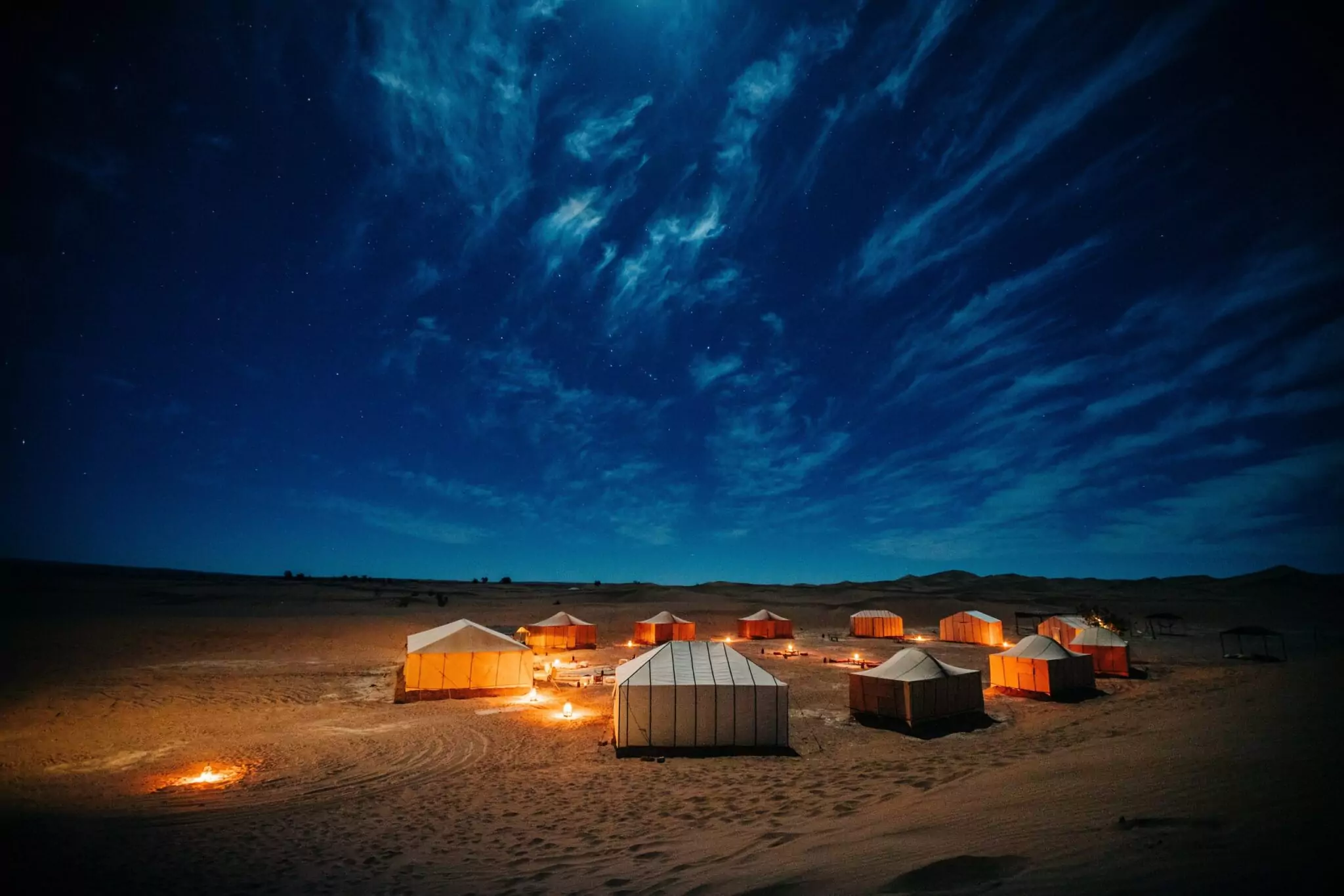 Luxury desert camp glowing amber beneath a starry Sahara sky near Merzouga — overnight desert tours in Morocco